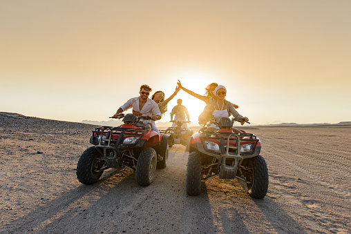 Young happy people driving quad bikes and having fun in the desert at sunset.