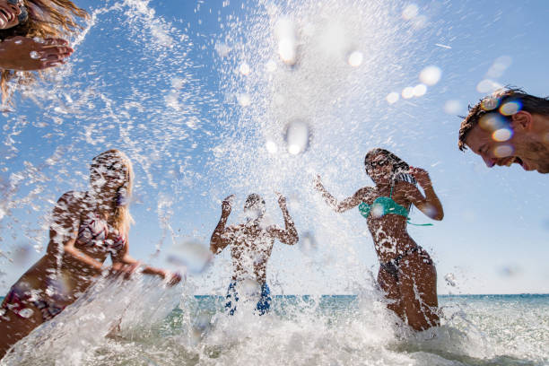 Cheerful friends having fun while running and splashing water during summer day at sea. Copy space.