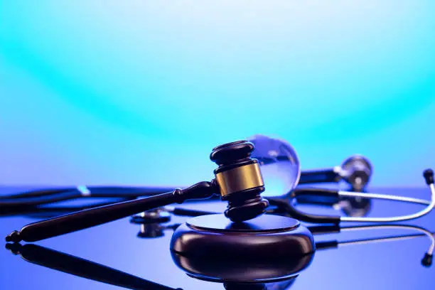 Gavel, legal code and stethoscope on the glass table. Blue light.