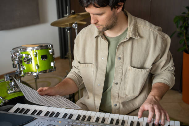 istock Man takes look at music sheet and plays notes on synthesizer 1409423503