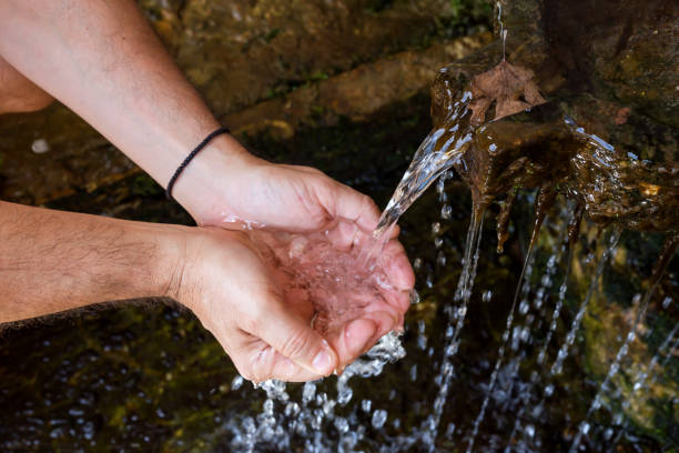 Living Water. In men's hands pouring cold, clear water from a source close-up.
