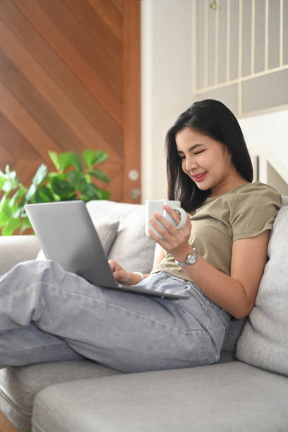 istock Beautiful asian woman sitting on couch and using laptop, remote working from home or spending time in social media. 1409424964