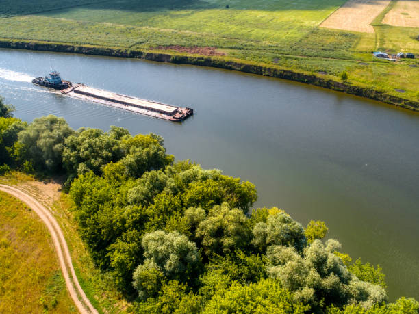 istock Small towboat pushes barge along calm water past fields 1409427087