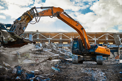 Modern excavator with hydraulic scissors cuts armored concrete beams working at abandoned industrial building demolition site