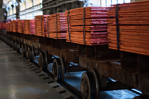 Stacks of cathode copper sheets tied with ribbons on rail carriages in light warehouse at metal refinery plant closeup