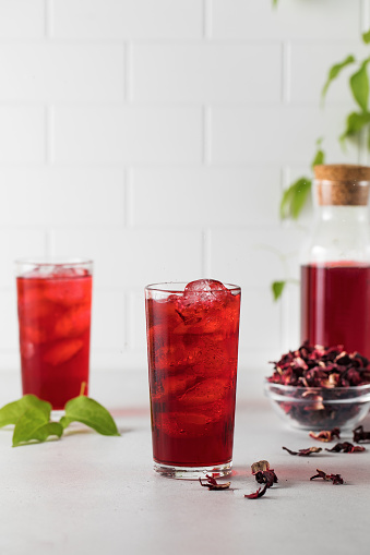 A refreshing drink made of dried hibiscus leaves and ice in a mug on a light background with shadows. Refreshing karkade tea.