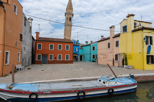 Colorful facades with vibrant colors and typical Venetian black and white wooden mooring pole in famous fishermen village on the island of Burano, Venice, Italy. Vessel and buildings reflecting in calm water. Beautiful poster like travel and tourism background on a sunny day with copy space.