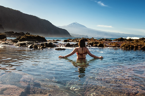 A girl stands in a natural pool in the Canary Islands, and in the background is the volcano Teide