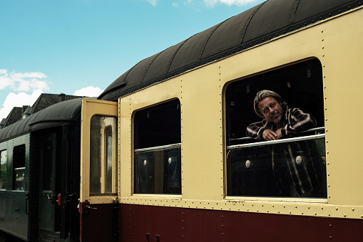 Blond man with stubble beard looking out window of a vintage train compartment. Seen from platform.