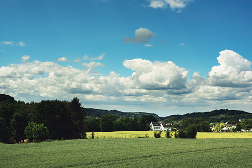 Houses in a rolling lush landscape in the countryside under a blue cloudy sky on a sunny summers day.