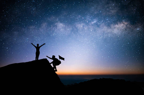istock Two young tourist with backpack is climbing a cliff with beautiful night sky, Milky Way and star over the sky. He had an effort to climb all the way to the top of the mountain and he had to succeed. 1409430128