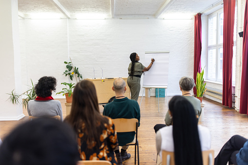 Business coach conducting training of businesspeople. African female professional discussing with audience and writing on flipchart during a seminar.