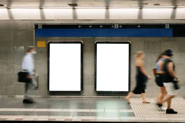 Two blank billboards in a subway station with commuters in blurred motion