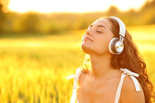 Woman meditating with headphones in a wheat field