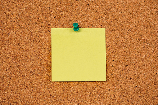 Empty single Yellow Post-it Sticky Notes on a cork board with drawing pi. Copy space