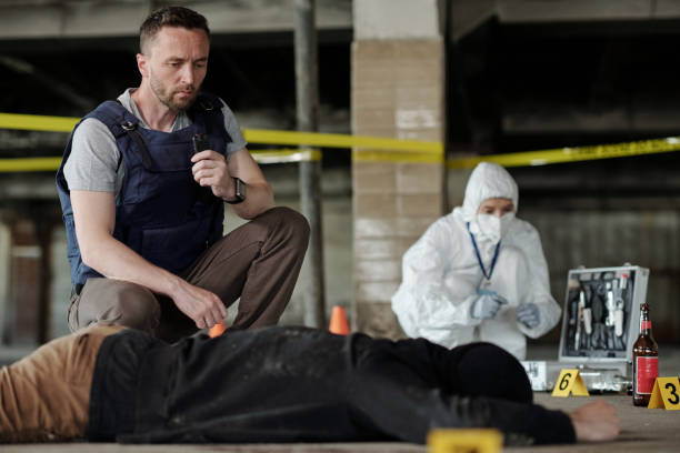 istock Young serious detective inspector or policeman squatting by dead body 1409436565