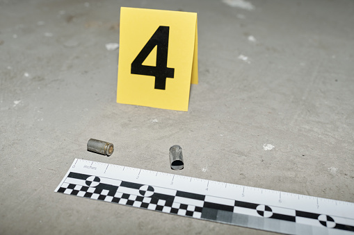 Yellow card with number four standing on asphalt by two empty cartridge cases left on crime scene shot from handgun of murderer
