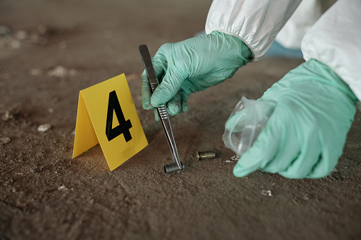 Hands of criminological expert holding empty cartridge case with metal pincers while putting it into plastic packet while seeking for evidences
