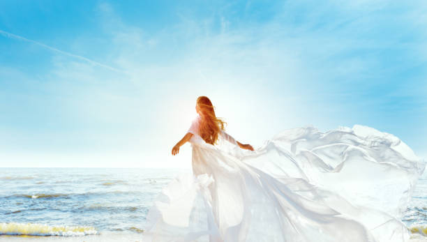 модель в белом платье летит на ветру. счастливая женщина, наслаждающаяся солнцем, смотрит в сторону на голубое небо. беззаботная девушка ме� - heaven women sunrise inspiration стоковые фото и изображения