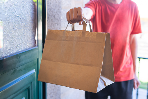 Man delivering a paper bag to the front door. Online shopping. Home delivery.