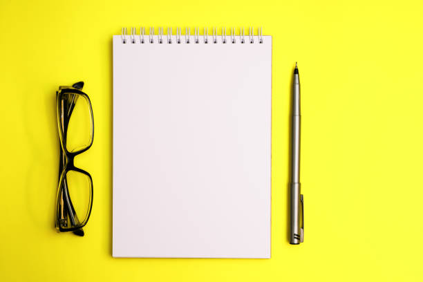 istock Top view on sketchbook and pen with eyeglasses on yellow background 1409442639