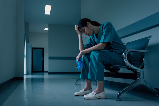 La enfermera médica está sentada en el pasillo del hospital en frustración y dolor después del fracaso y el concepto de condición corporal del paciente photo