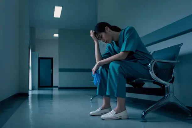 Medical nurse is sitting down a the hospital corridor in frustration and grief after failure and patient body condition