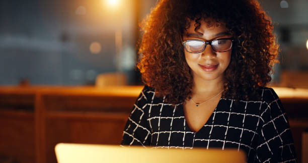 Black business woman using laptop, working late in modern office with copyspace. Smiling African American female working overtime, searching for new project. Lawyer using internet research or study