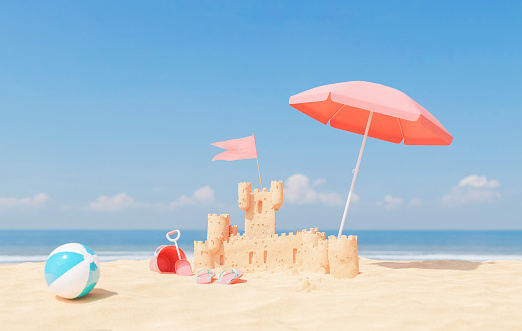 Sandy castle with umbrella and ball on seashore on sunny day