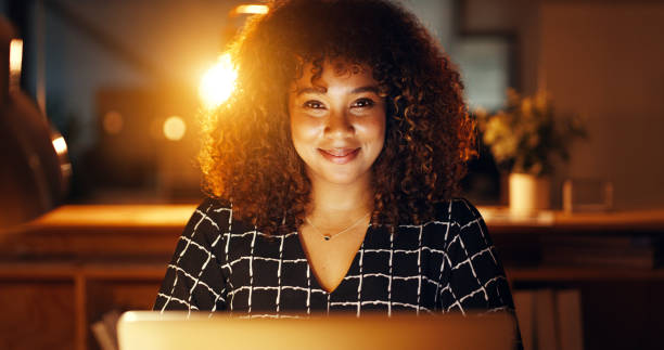 istock Ambitious and determined business woman with afro using technology for office startup. Smiling designer sitting overtime at night. Creative entrepreneur working late, using laptop to work on deadline 1409445328