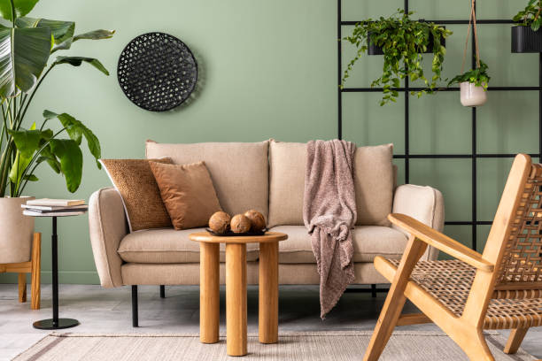 istock The stylish composition at living room interior with design beige sofa, coffee table, rattan armchair, plants and elegant personal accessories. Brown pillow and plaid. Cozy apartment. Home decor. 1409447111