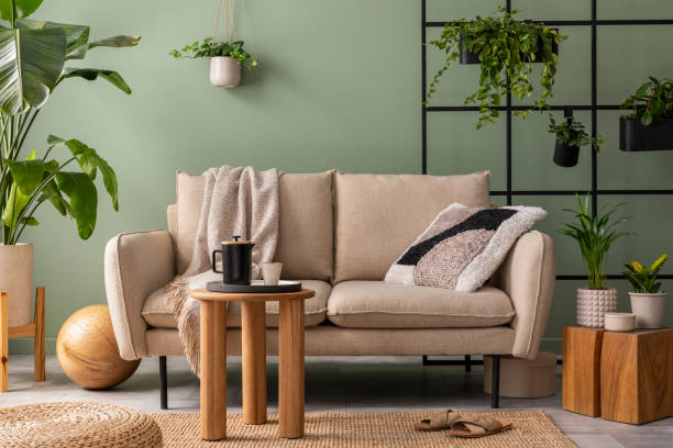 istock Modern composition at living room interior with design beige sofa, wooden coffee table, plants and elegant personal accessories. Brown pillow and plaid. Cozy apartment. Home decor. 1409447175