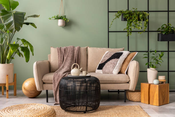 istock The stylish composition at living room interior with design beige sofa, black coffee table, plants and elegant personal accessories. Brown pillow and plaid. Cozy apartment. Home decor. 1409447240
