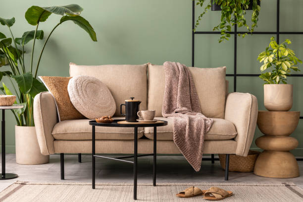 istock The stylish composition at living room interior with design beige sofa, black coffee table, plants and elegant personal accessories. Brown pillow and plaid. Green wall. Template. 1409447245