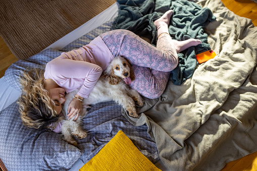 High angle view of young Caucasian woman in pajamas lying in the bed with her Cocker Spaniel dog