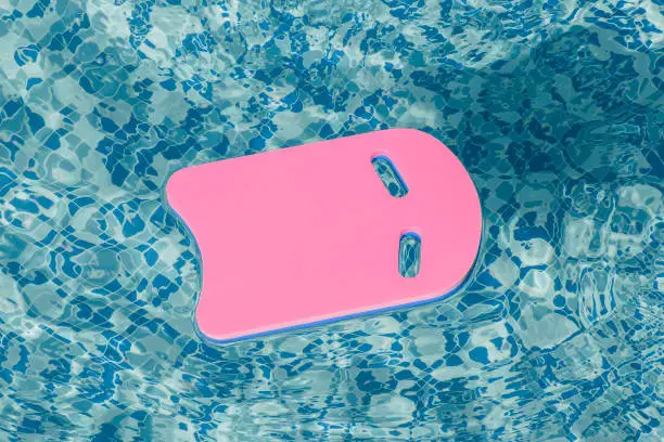Safe pool training aid float foam board tool. Pink Swimming kickboard on blue water surface of swim pool. Mockup, copy space for text or design. Water sport, active lifestyle