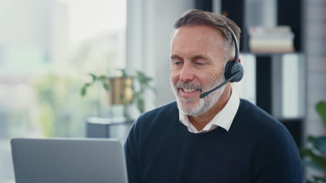 Business man on a video call conference using a headset. Professional IT manager or sales representative having friendly chat online with a client at home. Mature male consulting in a virtual meeting