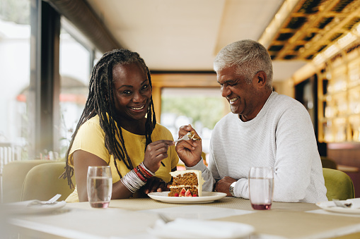 Mature couple smiling happily while sharing a delicious cake in a cafe. Carefree senior couple having a good time in a restaurant. Cheerful mature couple enjoying their retirement together.