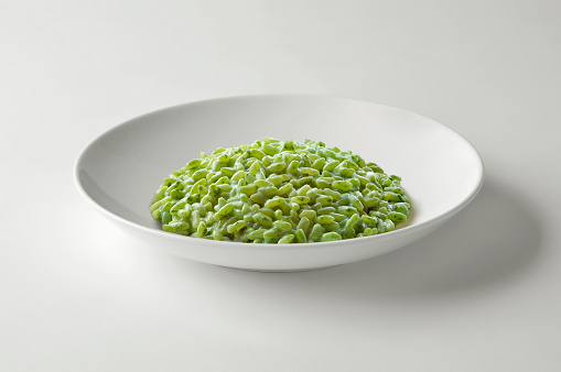 White bowl with green vegetable risotto isolated on white table