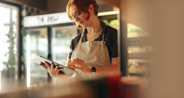 Cheerful store owner using a digital tablet in her grocery store Cheerful shop owner using a digital tablet while standing in her grocery store. Successful female entrepreneur running her small business using wireless technology. retail place stock pictures, royalty-free photos & images