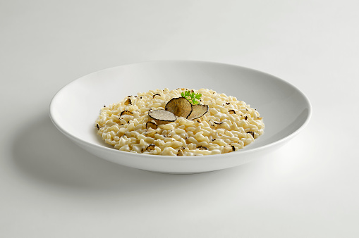 White bowl with risotto and slices of black truffle isolated on white table