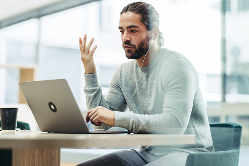 Businessman having a discussion with his associates during an online meeting. Modern businessman attending a video conference while working remotely in a co-working office.