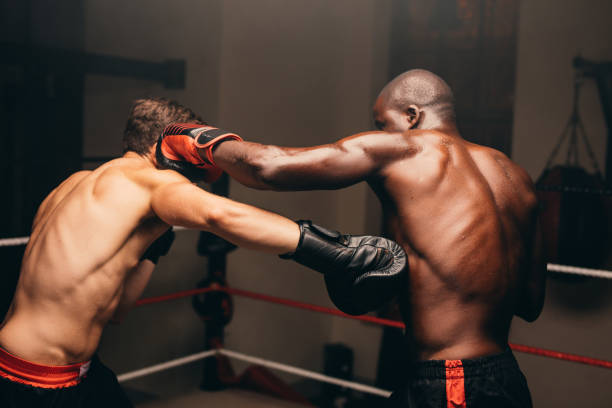 Two boxers fighting in a boxing ring Two multiracial boxers throwing punches during a fight in a boxing ring. Two athletic young men having a boxing match in a fitness gym. boxing stock pictures, royalty-free photos & images