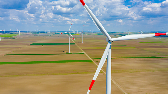 Above view on farm of large wind power turbines are standing among agricultural fields, generating clean renewable electrical energy for sustainable development.