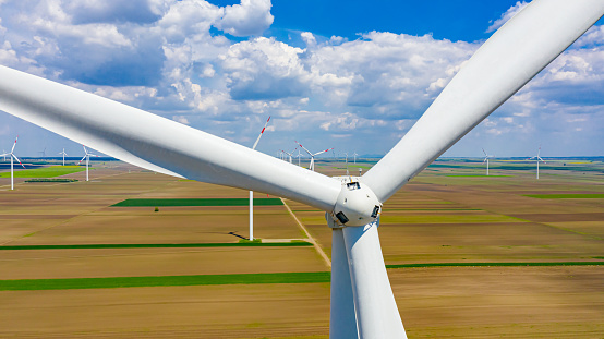 Close-up in aerial view at large propeller of windmill, wind generator, turbine, in background is field for producing renewable clean energy by converting kinetic energy on agricultural ground.