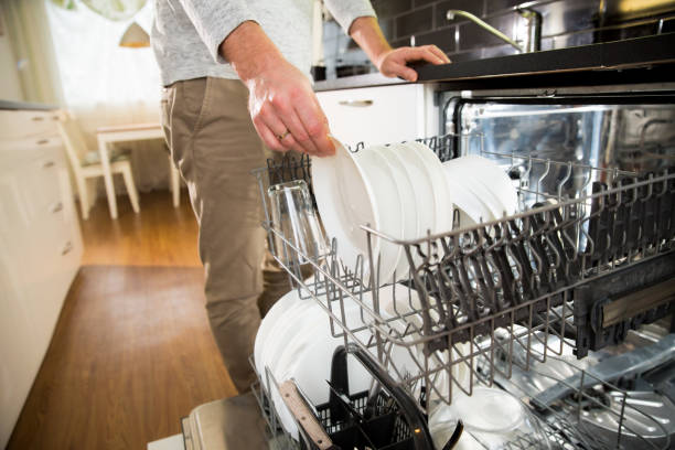A man taking clean dishes out of dishwasher. stock photo