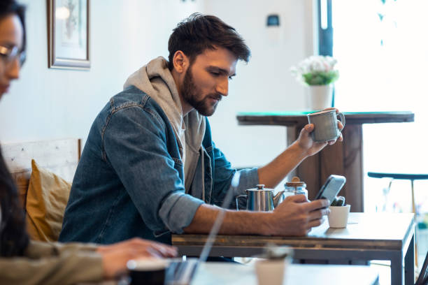 istock Handsome young man using his smartphone while drinking a cup o coffee in a eco bar. 1409454905