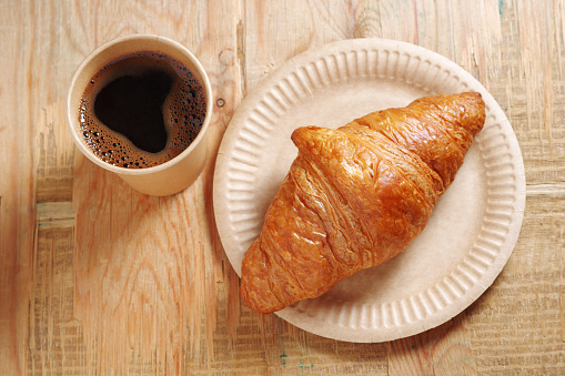 Disposable cup with coffee and croissant on old wooden background.
Biodegradable dishes