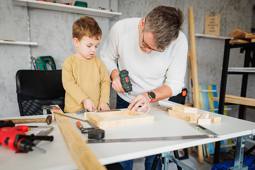 Father and son making wooden picture frame in carpentry workshop