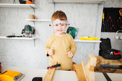 Little boy with protective eyewear in carpentry workshop looking at camera